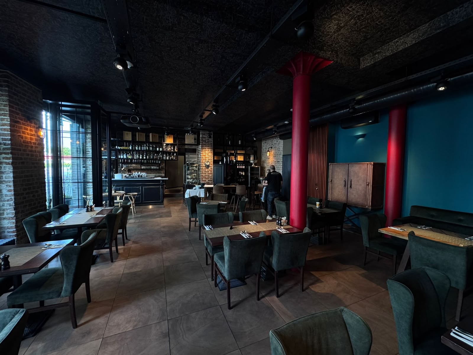 Der vordere Gastraum mit roten Säulen, grünen Sesseln und Blick zur Bar